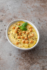 A bowl of hummus with chickpeas and basil on a table