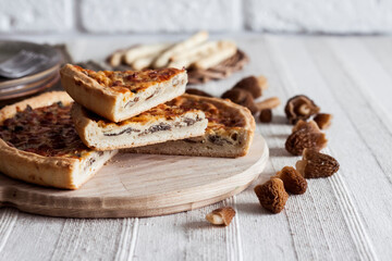 Quiche - open tart pie with morel mushrooms, onion and cheese on wooden cutting board
