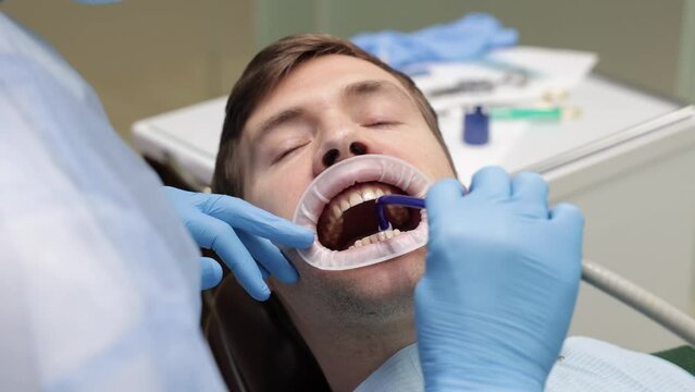 Man sit in a dental chair, saliva ejector in the mouth, caries treatment, dentist's gloved hands, dental retractor on the lips