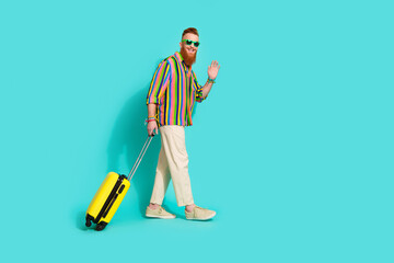 Full body length photo of bearded foxy guy in sunglass waving arm welcome to usa airport with luggage isolated on blue color background