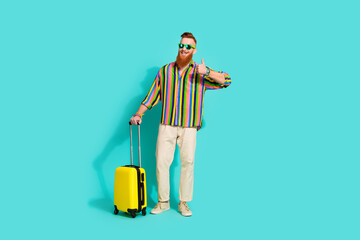 Full length photo of handsome businessman in striped shirt make like symbol thumb up his travel with baggage over cyan color background