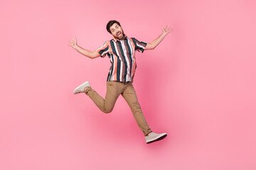 Fototapeta na wymiar Full length body size photo of energetic young brunet hair man jumping trampoline hands up overjoyed isolated on pink color background