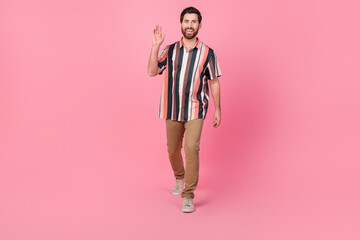 Full length photo of young man waving hand striped shirt and brown pants trendy look 2024 new collection isolated on pink color background