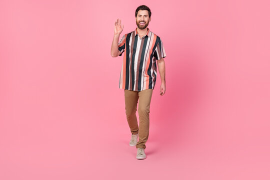 Full length photo of young man waving hand striped shirt and brown pants trendy look 2024 new collection isolated on pink color background