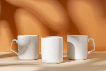 White ceramic mugs on peach background with shadows