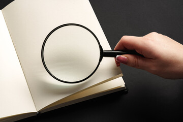 Notebook and magnifying glass on black background