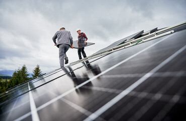 Technicians installing solar panel system on roof of house. Men workers in helmets carrying...