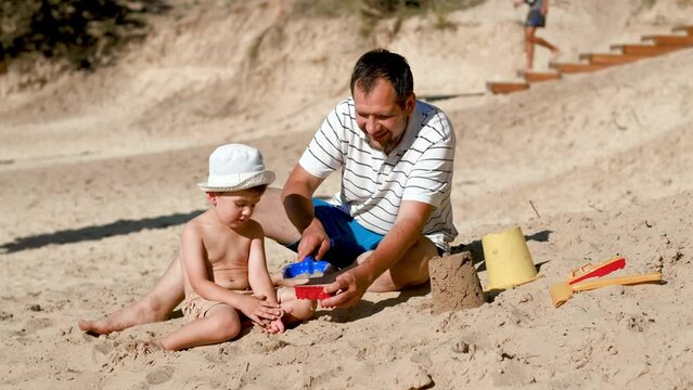 Father and 3 years son on beach building sand castle with plastic toys . single father solo parent. Involved parenting. Relaxing and playing outdoors with family