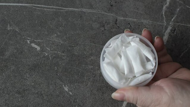 A woman opens a box of nicotine snus. Takes one pad and places it on the gray stone table.