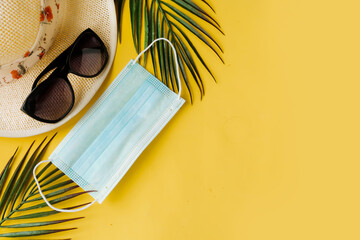 Straw hat, sunglasses and face medical mask on yellow background. Top view. Travel during the...