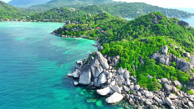 From above, witness the dramatic meeting of rocky shores and verdant woodlands, where the deep blue sea paints a picture of serene magnificence. Bird's eye view. Stock footage. Koh Tao, Thailand. 4K.
