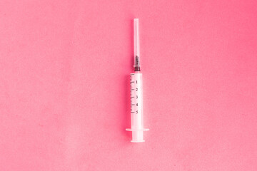 Medical syringe on pastel pink background. Top view, minimal