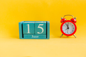 June 15. Blue cube calendar with month date and alarm clock on bright yellow background