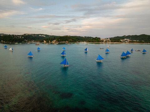 Turquoise water with paraw sailing, tourist boats, and sunset cruise in Boracay. Philippines.