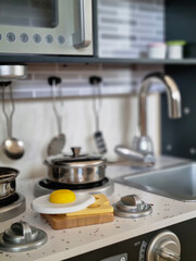 Toy kitchen in the baby's room. Toy kitchen utensils and wooden meal. Dirty dishes in a sink. Cooking pots over cooking stove.