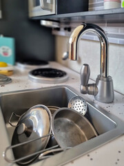 Toy kitchen in the baby's room. Toy kitchen utensils and wooden meal. Dirty dishes in a sink. Cooking pots over cooking stove.
