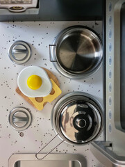 Toy kitchen in the baby's room. Toy kitchen utensils and wooden meal. Dirty dishes in a sink. Cooking pots over cooking stove.