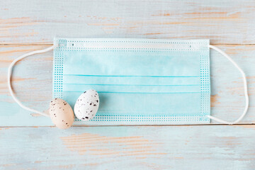 Color quail eggs in face medical mask on wooden background. Coronavirus easter concept