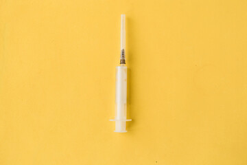 Medical syringe on bright yellow background. Top view, minimal