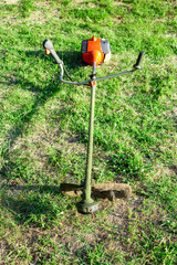 petrol mower with fishing line on the grass in the garden on a summer day. Mowing the grass, maintaining the garden