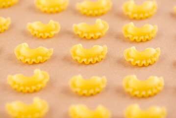 Pattern raw Creste Di Gallo pasta on a beige background. Rooster scallop.