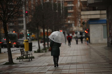 Mid aged woman with white umbrella walks a rainy city street in the rain|