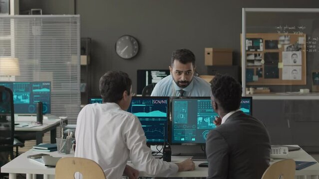 Medium shot of three multiethnic male cybersecurity officers discussing data info on network computer program while co-working in office