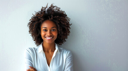 A beautiful smiling african american woman with curly hair in a white shirt standing against a gray wall, copy space for text banner