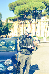 Happy smiling bearded man standing near a car at Rome,Italy.Man holding a mobile phone standing outdoors next to his car texting ,sending parking sms