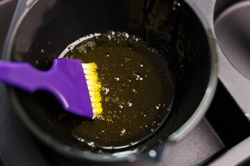 A purple brush is submerged in a pot of liquid mixture