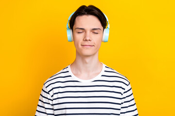 Photo of calm student dressed striped t-shirt listen music chill playlist in headphones close eyes isolated on yellow color background