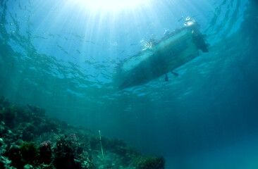 Boat from underwater with sunrays and reef below. 