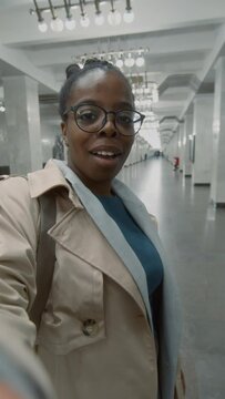 Vertical POV UGC of African American travel blogger in glasses and trench coat recording video telling about riding subway in new place