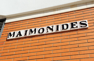 Maimonides. Rótulo de calle con azulejos típicos sevillanos con letras negras sobre fondo blanco en un muro de ladrillos rojos. Sevilla, España
