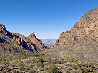 Fototapeta na wymiar A desert valley in between two mountains and rock formations in Big Bend National Park in Texas. This landscape has a narrow view and clear blue skies for a remote Southwest destination.