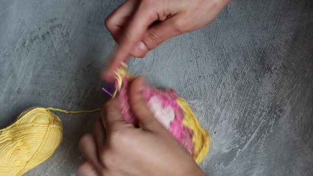 Female hands holding crochet hook and square ornament. Crochet pattern close up. Woman crochets geometric shape ornament using cotton yarn. Space for text. 