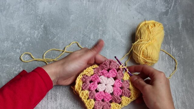 Female hands holding crochet hook and square ornament. Crochet pattern close up. Woman crochets geometric shape ornament using cotton yarn. Space for text. 
