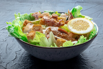 Caesar salad with chicken breast, lettuce, croutons, and a lemon, on a slate background - 746527961