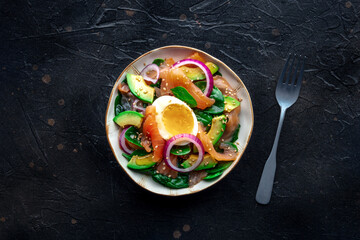 Salmon, avocado and egg salad with fresh leaves and onions, overhead flat lay shot on a black slate background, with a fork. Healthy diet - 746528101