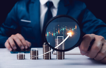 Businessman analyzes growth with magnifier over coins and graph. Stock market, Business growth,...