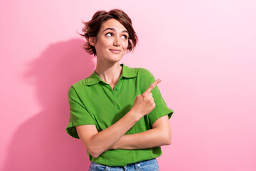 Photo of charming thoughtful young lady wear green shirt looking pointing finger empty space isolated pink color background