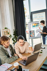 Fototapeta premium smart startup team members discussing project and working on laptops in coworking space, men in 20s