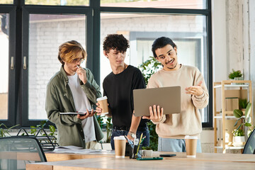 Three young men engaged in a lively discussion over a laptop at a coworking space, startup ideas