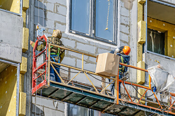Workers are engaged in finishing the facade of an apartment building under construction on a winter...
