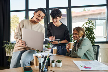 young man presenting his ideas while holding laptop and talking to startup team during brainstorming