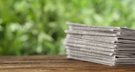 Stack of newspapers on wooden table against blurred green background, space for text. Journalist's work - obrazy, fototapety, plakaty