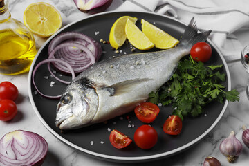Fresh dorado fish and ingredients on white marble table