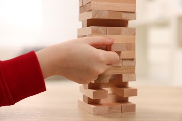 Child playing Jenga at wooden table indoors, closeup