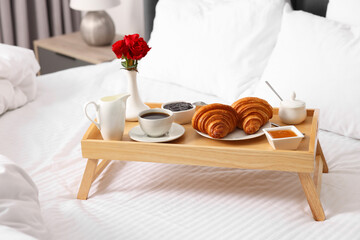 Wooden tray with tasty breakfast on bed at home