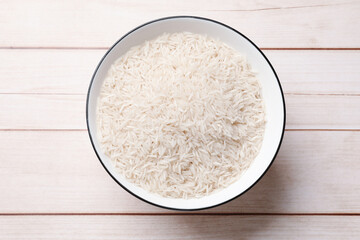 Raw basmati rice in bowl on white wooden table, top view